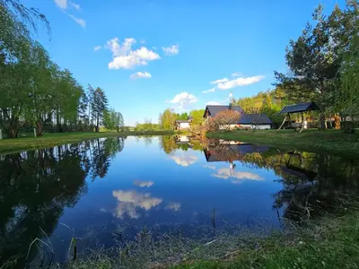 a river with a house in the background and a reflection in the water at Pakalnės sodyba in Skverbai