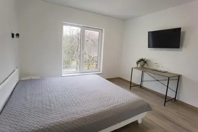 a white bedroom with a bed and a television at Pakalnės sodyba in Skverbai