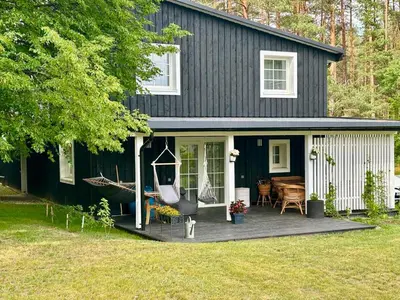 a black house with a porch with a hammock at Pušyno apartamentai in Druskininkai