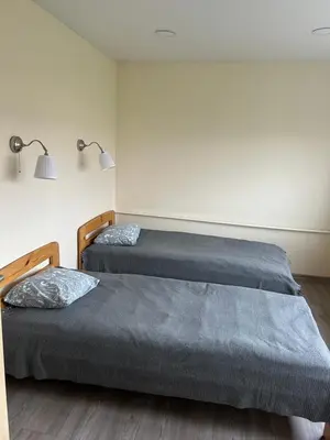 two beds in a room with two lamps on the wall at White apartment in Druskininkai