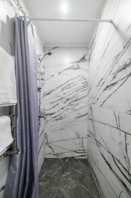 a bathroom with white marble walls and a shower at Fox studio apartment in Šiauliai