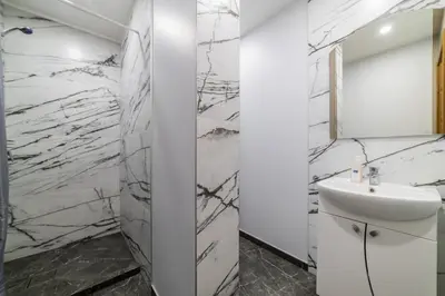 a bathroom with white marble walls and a sink at Fox studio apartment in Šiauliai