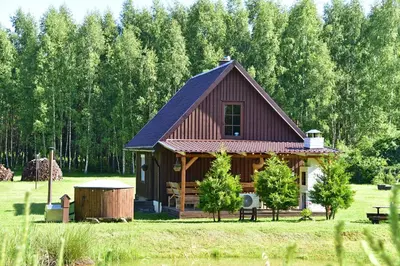 a cabin in a field with trees in the background at Pundeliškių sodyba in Šalčininkai
