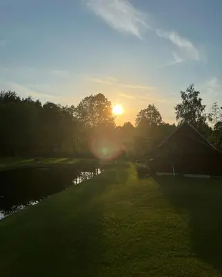 a sunset over a river with a house and trees at Stripeikių Bitė in Varniškės I