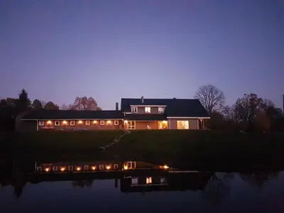 a house with lights on the water at night at Villa Cheval in Aukštadvaris
