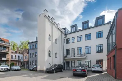 a white building with cars parked in a parking lot at Serene Nemunas River View apartment near McDonald by Polo Apartments in Kaunas