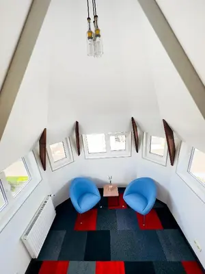 an attic room with two blue chairs and a table at Broken bed hootel in Kaunas
