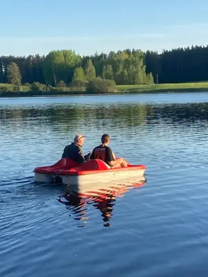 two people sitting on a red boat on a lake at Našio kempingas in Antanaše