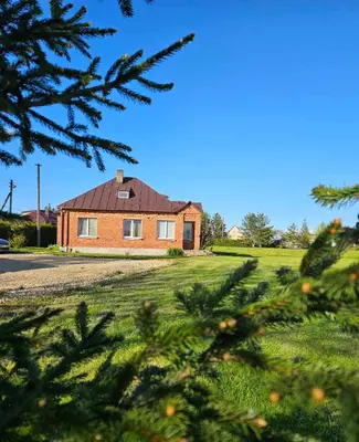 a brick house in a field with trees in the foreground at Red Brick House in Naciūnai