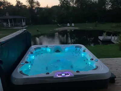 a hot tub sitting on a deck next to a pond at Žalčio guolis in Lekėčiai