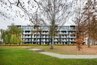 a building in front of a park with trees at Nemunas Park Apartment in Prienai