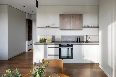 a kitchen with white walls and wooden cabinets at Nemunas Park Apartment in Prienai