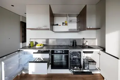 a kitchen with white cabinets and black appliances at Nemunas Park Apartment in Prienai