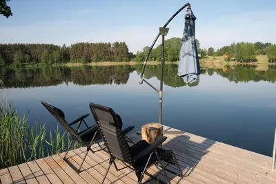 two chairs and an umbrella on a dock next to a lake at Pineplace trio KOPA in Žaugėdai