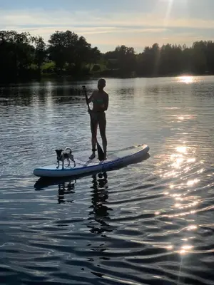 a man and a dog on a paddle board in the water at Pineplace trio JŪRA in Žaugėdai
