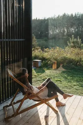 a woman sitting in a rocking chair reading a book at Konga Stay M - Private Jacuzzi Included in Strakiškiai