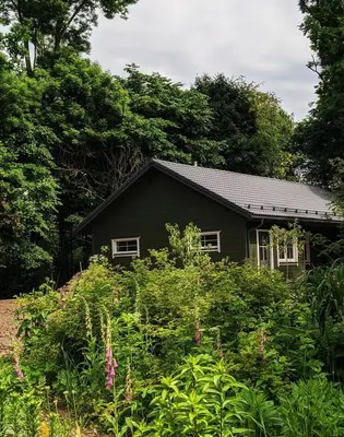 a small black house in the middle of a garden at Svečių namelis KNYGŲ NAMAS in Kelmė