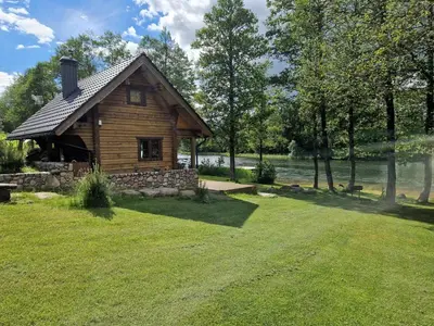 a log cabin on a lawn next to a lake at Pirtis su ežero pakrante Trakai in Salkininkai