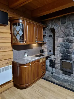 a kitchen with wooden cabinets and a stone fireplace at Pirtis su ežero pakrante Trakai in Salkininkai