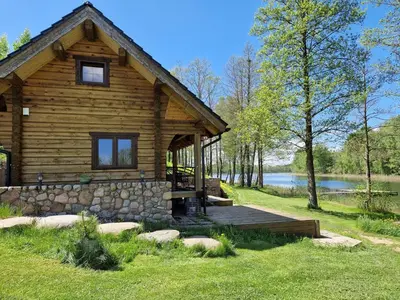 a log cabin with a stone wall next to a lake at Pirtis su ežero pakrante Trakai in Salkininkai