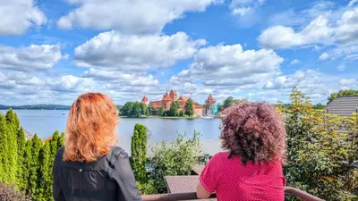 two women sitting on a bench looking at a lake with a castle at Trakai Castle View Villa55 in Trakai