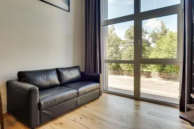 a leather couch in a living room with a large window at Uptown Lofts in Vilnius