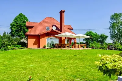 a house with a red roof on a green lawn at Tytuvos upelio Krantinė in Tytuvėnai