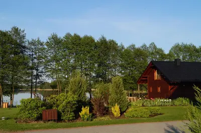 a red barn in a garden with a lake at Vila Viesai in Trakai
