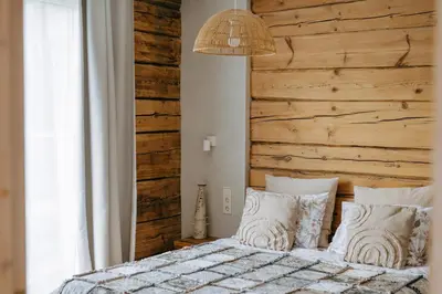 a bedroom with a wooden wall and a bed with pillows at Upės Namai Jonami in Anykščiai