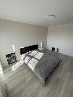 a white bedroom with a bed and a wooden floor at Karoliniškių apartamentai in Vilnius