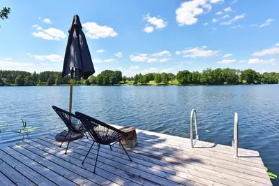 an umbrella and chairs on a dock on a lake at Pineplace trio BANGA in Žaugėdai