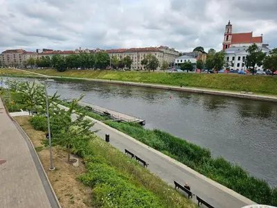 a river with benches next to a road and buildings at Modern Apartment near Old Town & River in City Center in Vilnius