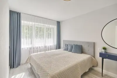 a white bedroom with a bed and a window at Apartamentai Vilniaus alėjoje in Druskininkai
