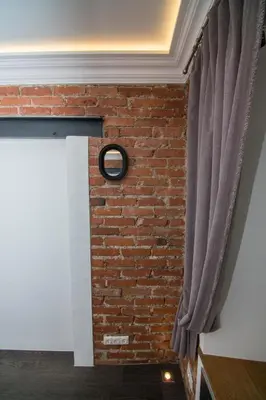 a brick wall with a window and a curtain at Modernios klasikos studija in Kaunas