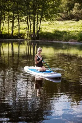 a woman sitting on a paddle board in the water at Shanti Resort - Retreat & Wellness Center in Sarboriškės I