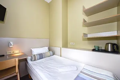 a small room with a bed and a desk and shelves at Nykščio Hostel in Anykščiai