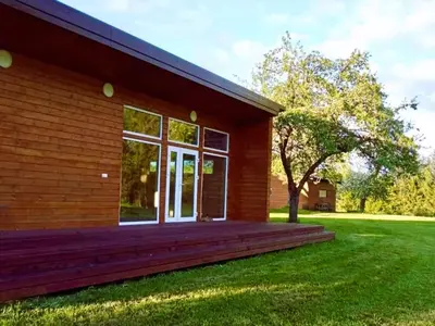 a house with a large wooden porch on a green lawn at Raimundėlio sodyba in Rokiškis