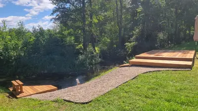 a wooden deck next to a river with a bridge at Varėnės sodyba in Vėžionys