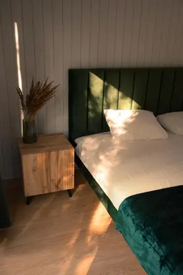 a bed with a green headboard and a night stand at Miško terapija in Kriviliai