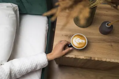 a person holding a cup of coffee on a table at Miško terapija in Kriviliai