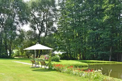 a park with two chairs and an umbrella next to a pond at Bražuolėje Pas Juozą- ramiam poilsiui in Trakai