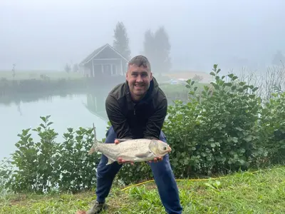 a man holding a fish in front of a lake at Pas Žuvelį in Stariai