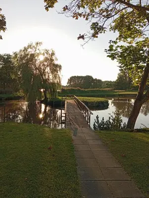 a walkway next to a river with a bridge at Sodyba Prie Tvenkinio in Kurtuvėnai