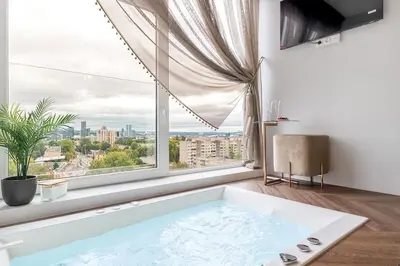 a bath tub in a room with a large window at Vega - Whirlpool - Self Checkin in Vilnius