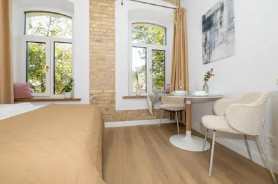 a bedroom with a bed and a table and two windows at cohost I Brand New Apt, w-AC in a Central Location in Vilnius