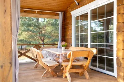 a table and chairs on a porch with a window at Pine Valley Villa - beautiful nature, jacuzzi, sauna, cozy log house in Inturkė