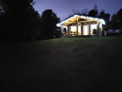a small house with lights on a field at night at Pine Valley Villa - beautiful nature, jacuzzi, sauna, cozy log house in Inturkė