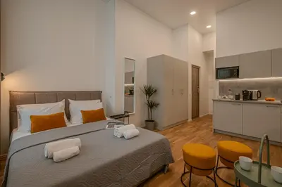 a bedroom with a large bed with two chairs and a kitchen at Railway Apartments in Vilnius