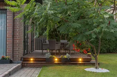 a patio with a table and chairs under a tree at Luxury villa with sauna in the pine forest close to Vilnius city centre in Vilnius