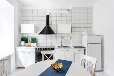 a white kitchen with white appliances and a table at Cosy and bright Saint Ignoto Apartment by Reside Baltic in Vilnius